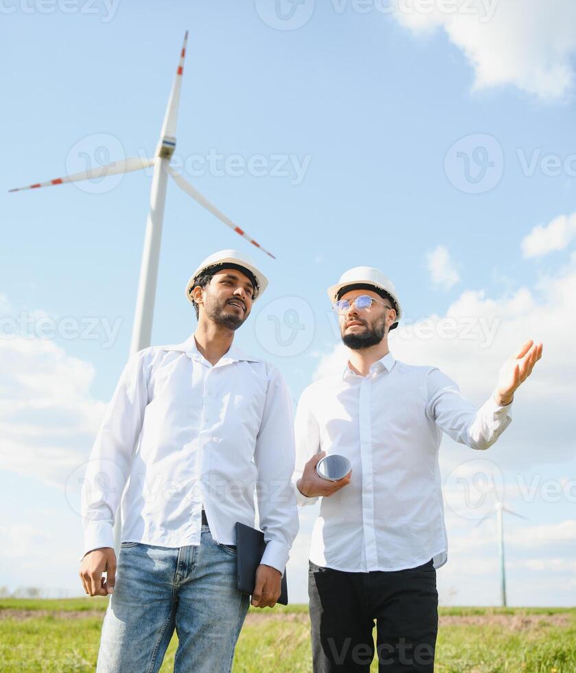 Two engineers discussing against turbines on wind turbine farm. photo