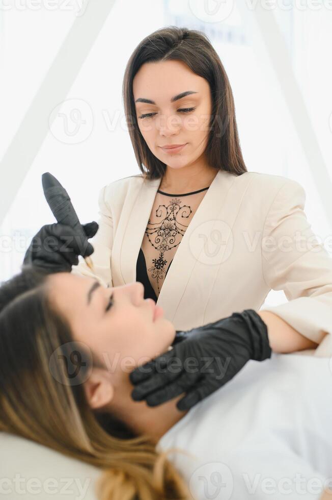 Cosmetologist applying permanent make up on eyebrows- eyebrow tattoo photo