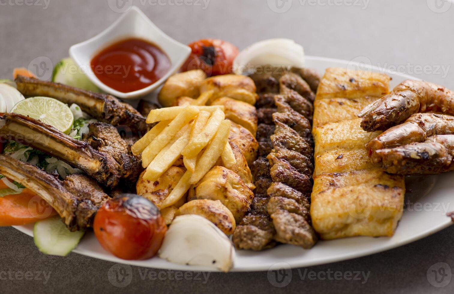 persian mix grill platter with tikka boti, lamb chop, meat kabab, fish, fries and tomato sauce served in dish isolated on grey background top view of arabic food photo