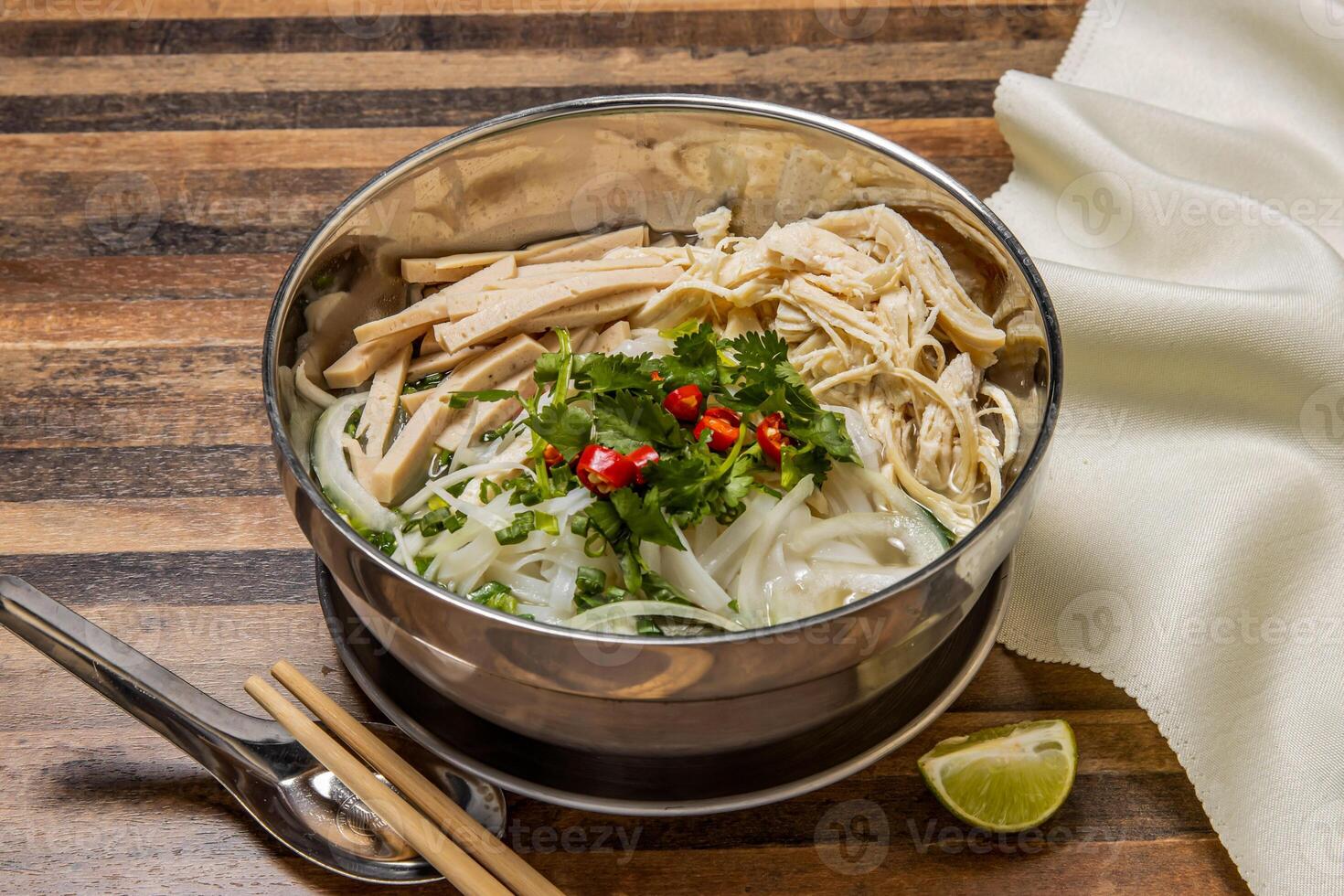 Shredded Chicken and Sausage Pho topping with noodles, spring onion, red chilli, coriander and chopsticks served in bowl isolated on wooden table top view of hong kong fast food photo