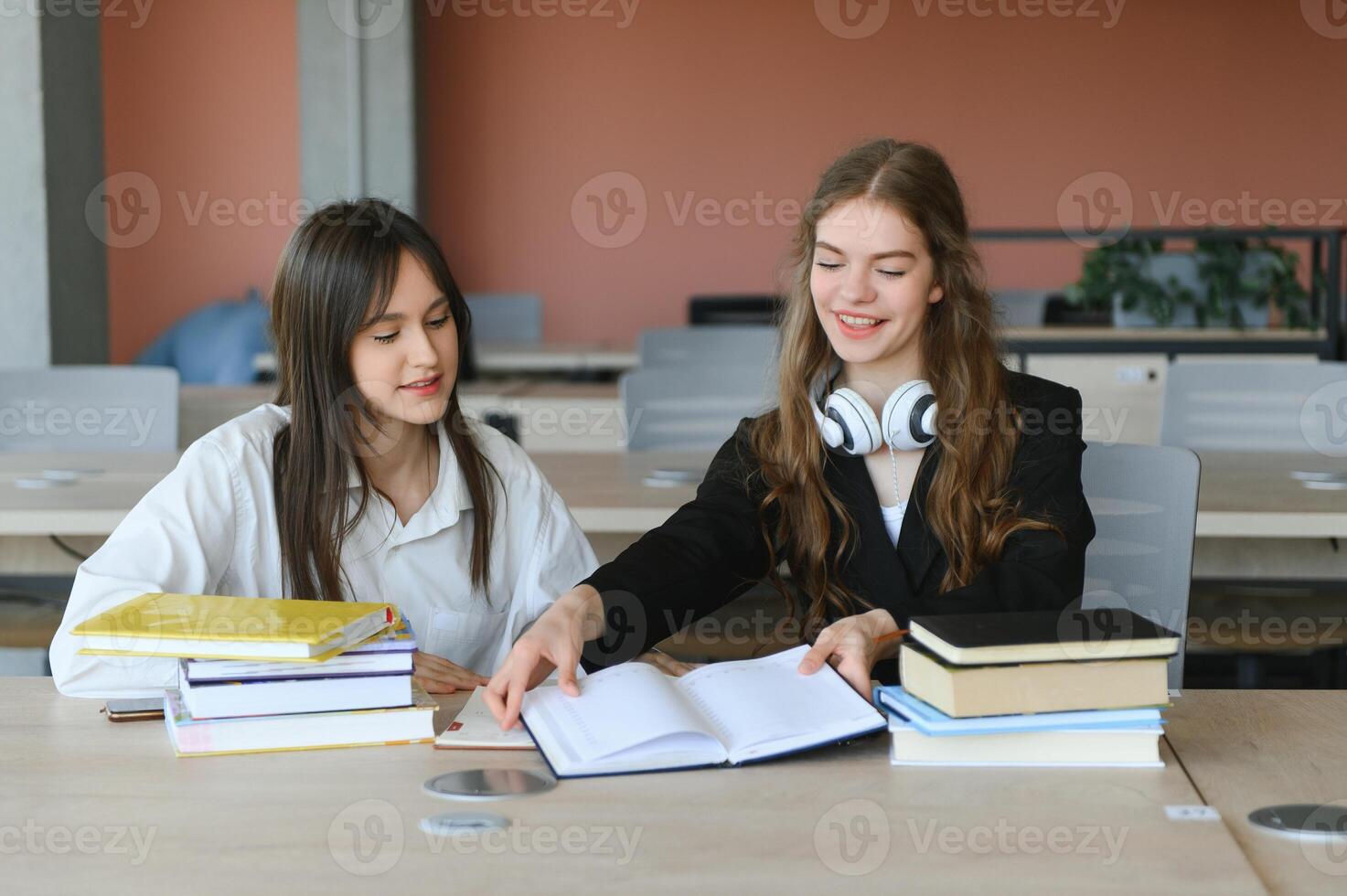 Two fifteen-year-old schoolgirls reading books and taking abstract in copybooks are doing homework in the school library photo