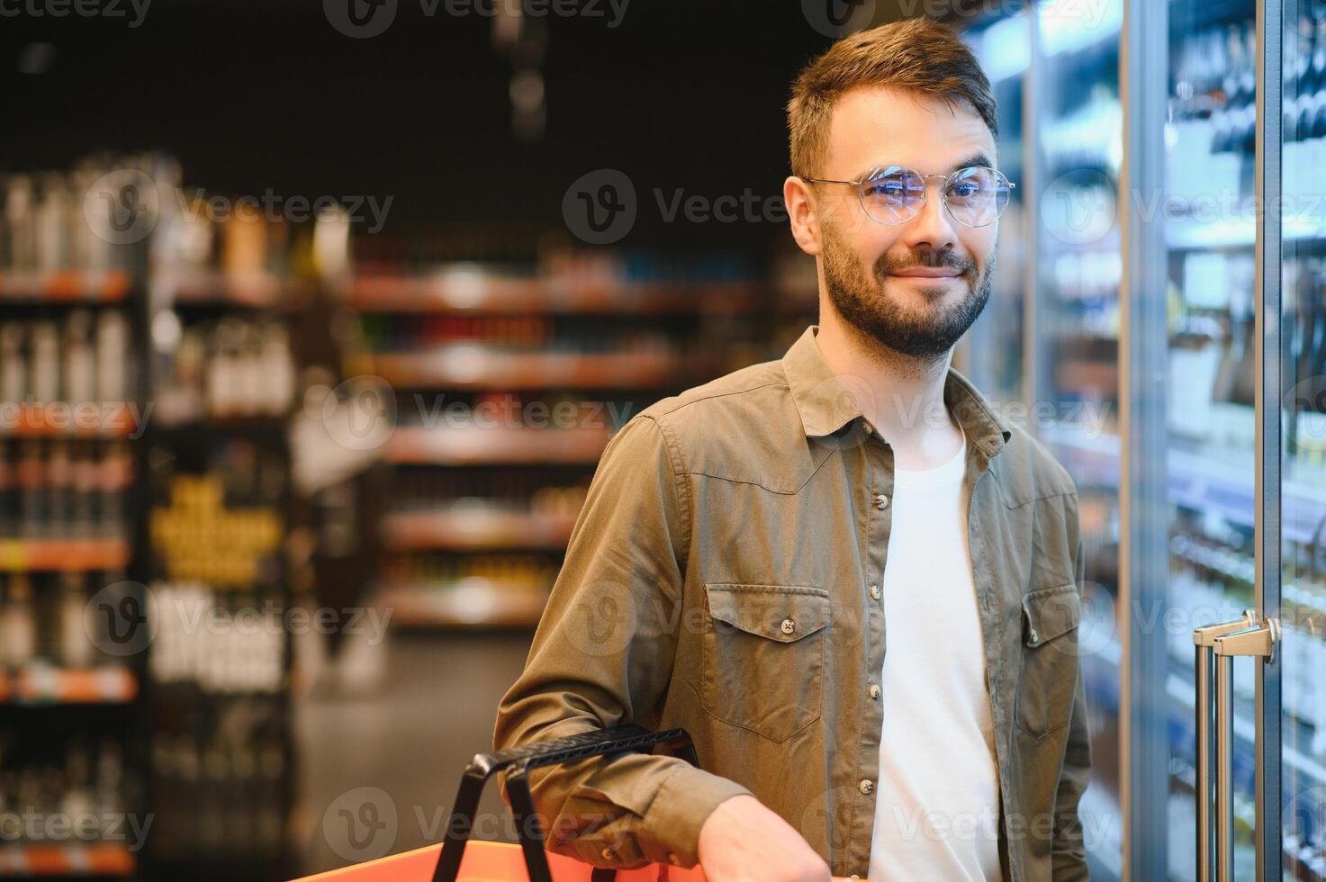 Man with a beard buys a beer in the alcohol department of a supermarket . Handsome man chooses a beer bottle in the store and communicates on a smartphone.Shopping in a supermarket photo