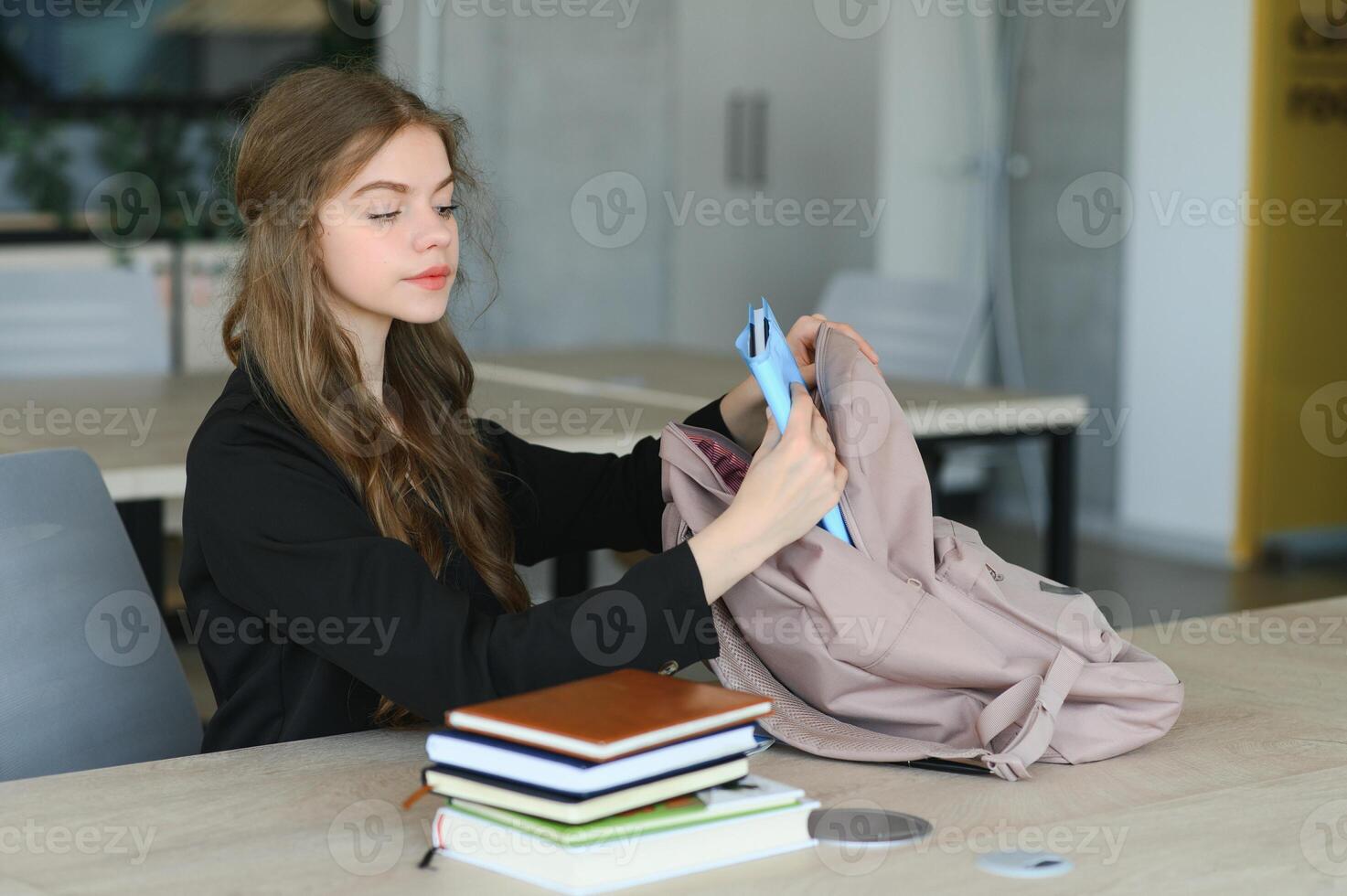 A cute 15-year-old schoolgirl sits at a school desk with notebooks and books and studies photo