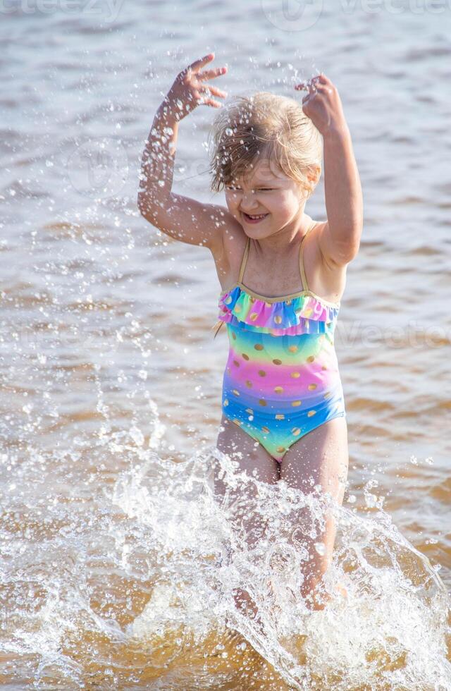 joven contento niño niña de europeo apariencia años de 6 6 teniendo divertido en agua en el playa y salpicaduras, tropicales verano vocaciones,vacaciones.a niño disfruta el mar.vertical foto. foto