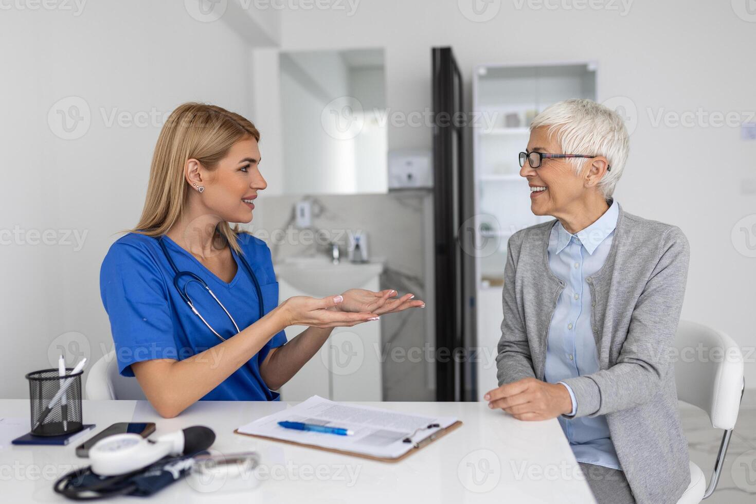 Young woman doctor or GP in white medical uniform consult female patient in private hospital. Female therapist speak talk with senior woman client on consultation in clinic. photo