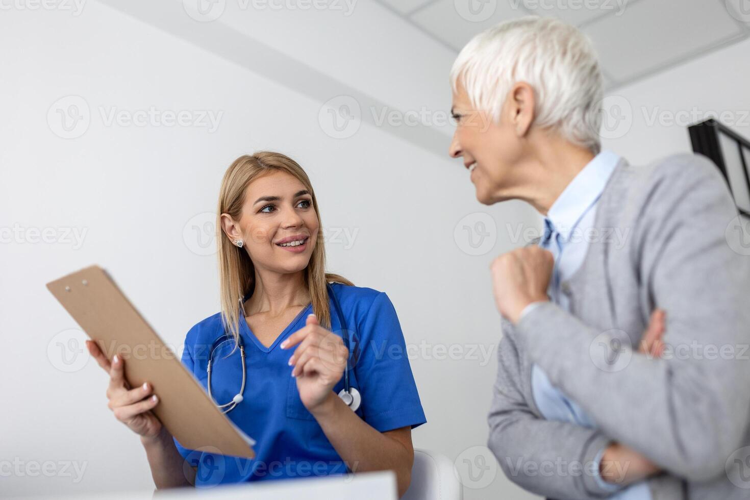 Young woman doctor or GP in white medical uniform consult female patient in private hospital. Female therapist speak talk with senior woman client on consultation in clinic. photo