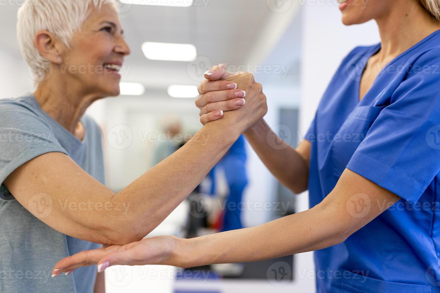 Caregiver helping contented senior woman exercise at clinic. Rehab for elder, senior medical care. Elder woman returning to good state of health photo