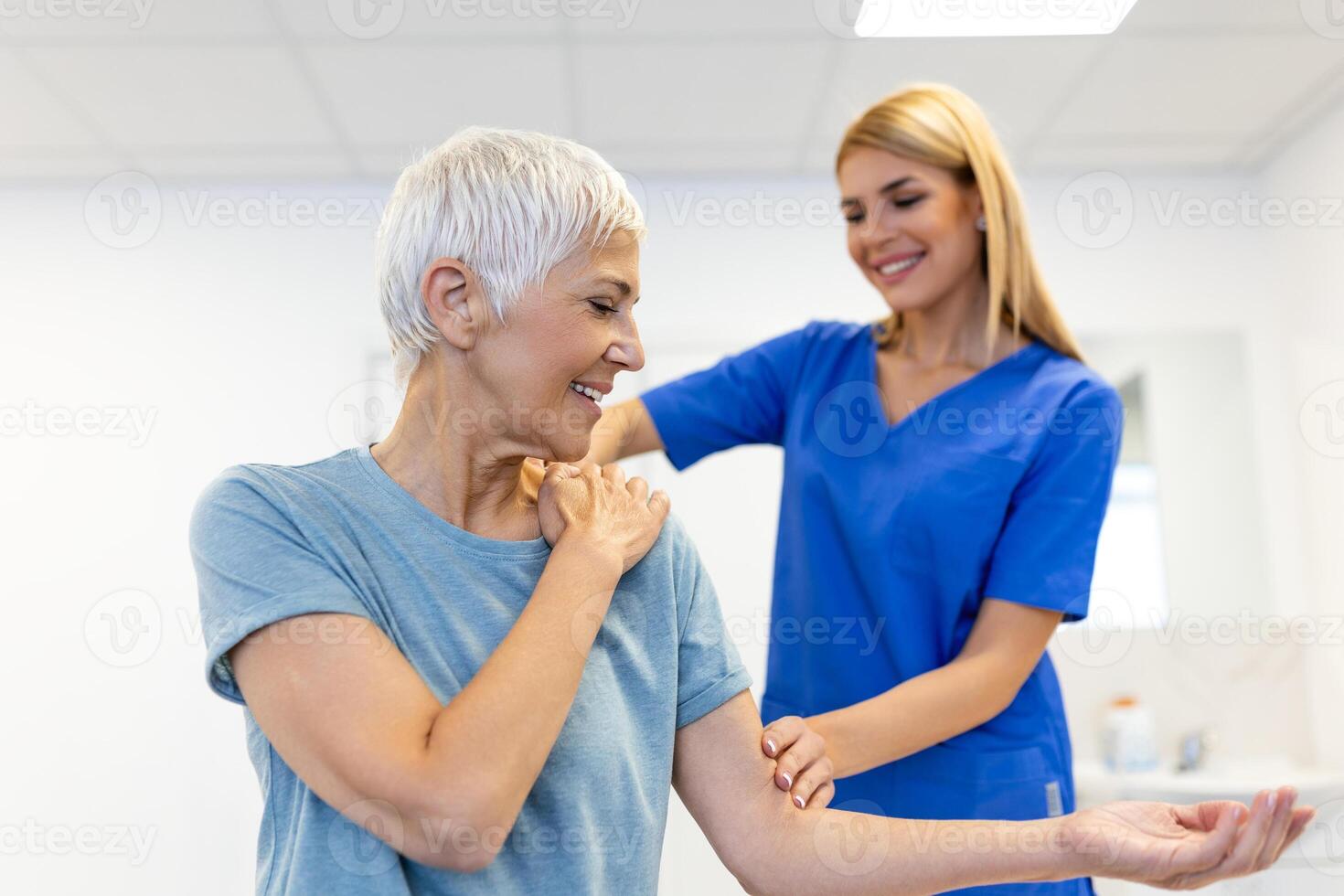 Caregiver helping contented senior woman exercise at clinic. Rehab for elder, senior medical care. Elder woman returning to good state of health photo