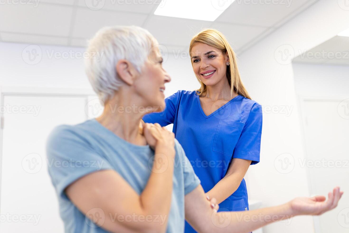 Caregiver helping contented senior woman exercise at clinic. Rehab for elder, senior medical care. Elder woman returning to good state of health photo