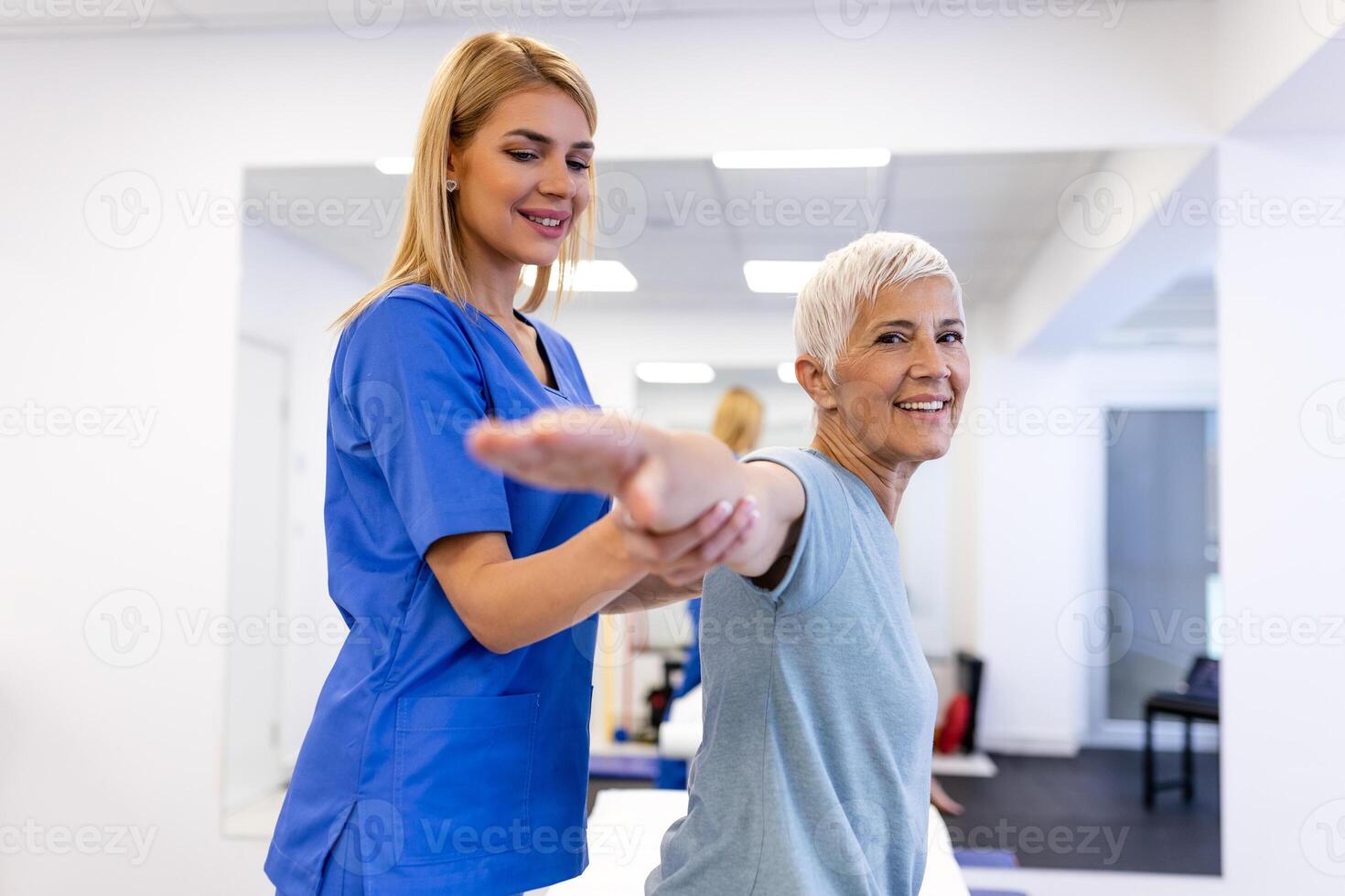 Doctor orthopedic teaching senior woman to do osteoporosis treatment exercise in modern clinic. Physiotherapist helping female patient during muscle rehabilitation physiotherapy photo