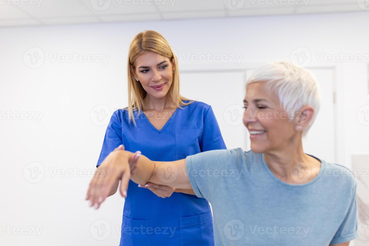 Caregiver helping contented senior woman exercise at clinic. Rehab for elder, senior medical care. Elder woman returning to good state of health photo