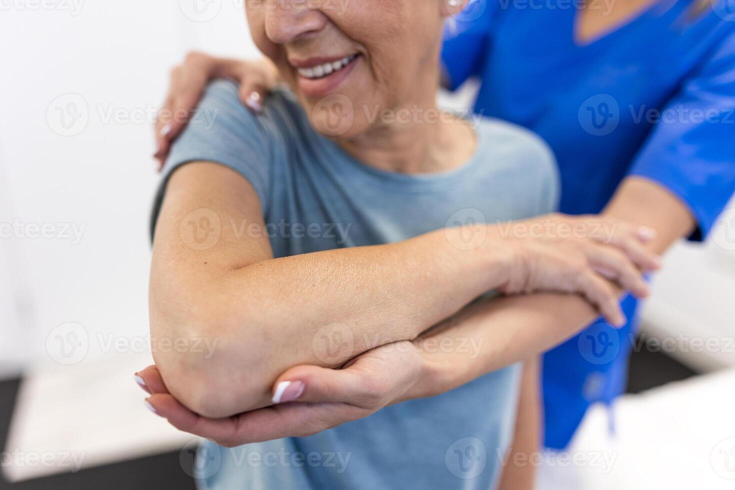 Happy senior woman doing exercise with physiotherapist. Old retired lady doing stretching arms at clinic with the help of a personal trainer during a rehabilitation session. photo