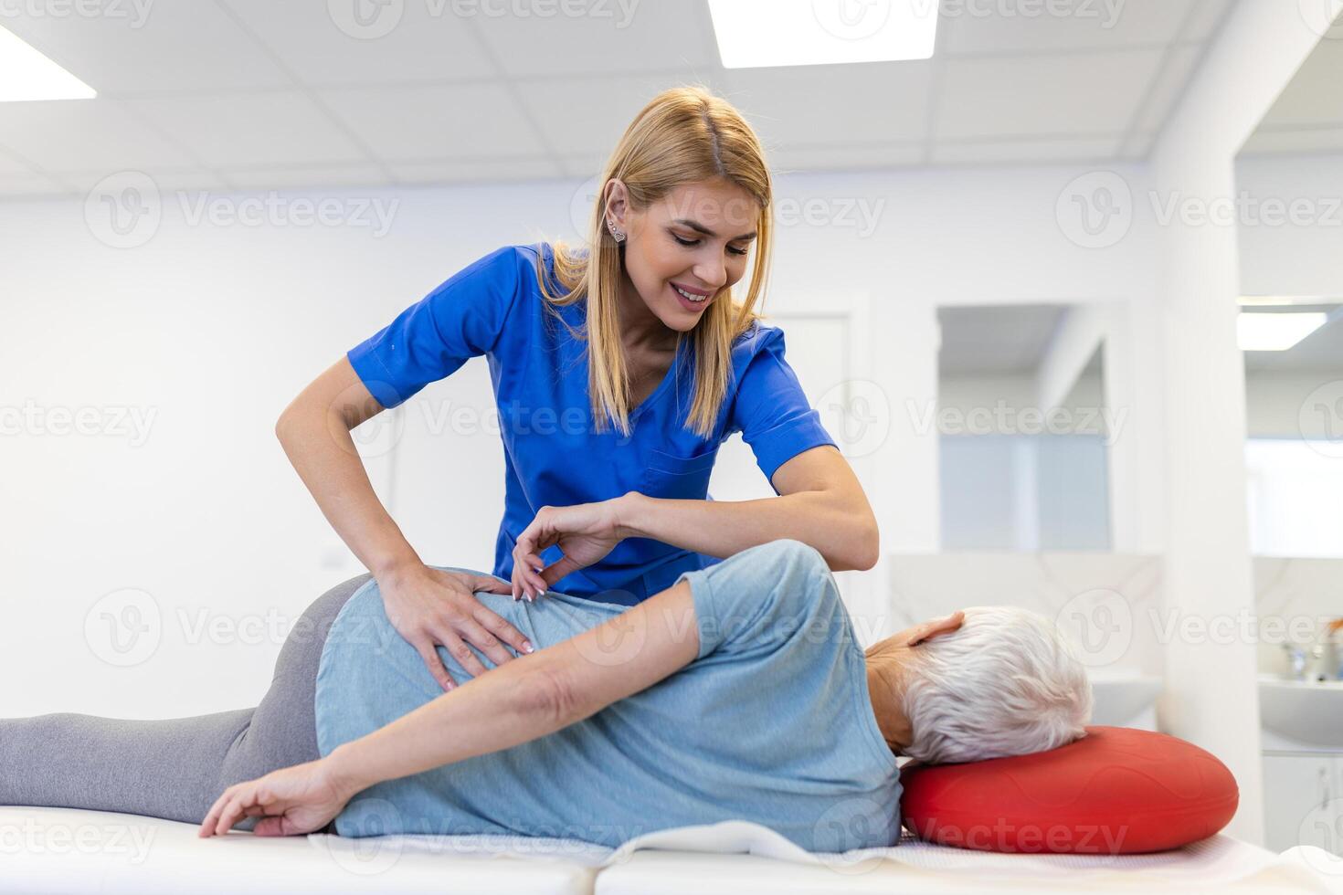 Young doctor chiropractor or osteopath fixing lying senior woman back with hands movements during visit in manual therapy clinic. Professional chiropractor during work photo