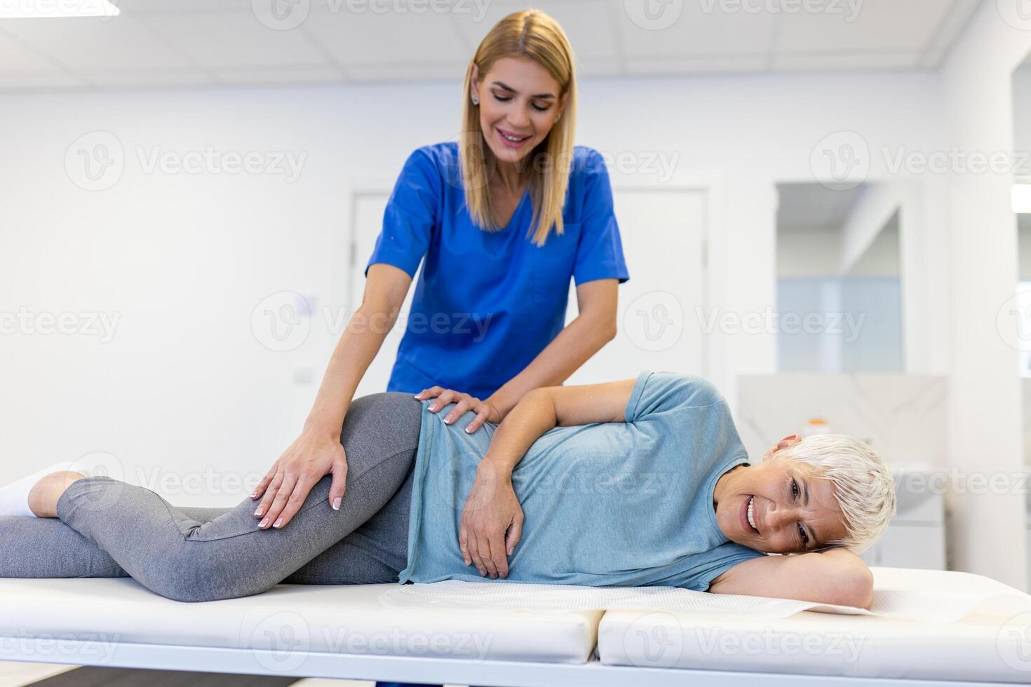 Young doctor chiropractor or osteopath fixing lying senior woman back with hands movements during visit in manual therapy clinic. Professional chiropractor during work photo