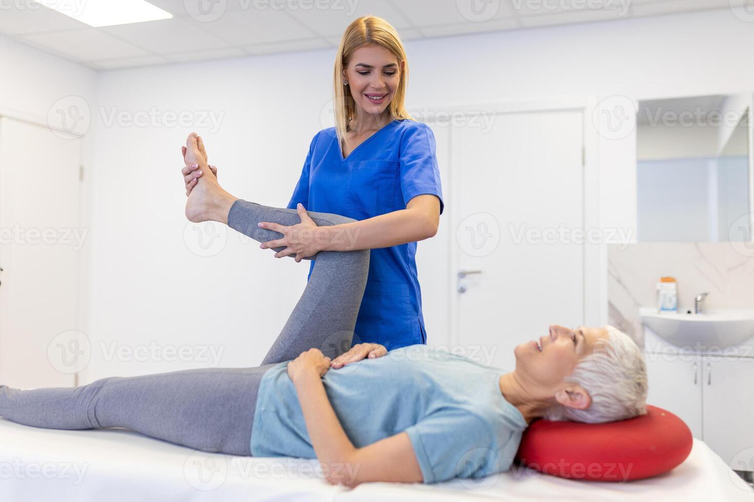close up of female physiotherapist is helping senior elder woman stretching her hamstring and doing thigh or leg rehabilitation in exercise room - she is lying on massage bed photo
