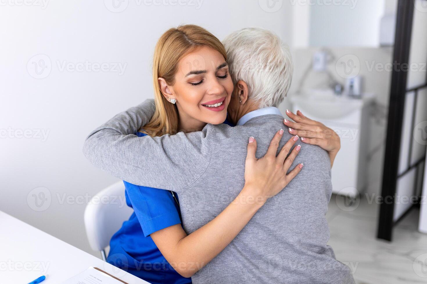 The elderly woman enjoys an embrace from her favorite healthcare doctor. Medical care, young female doctor hugging patient. Empathy concept. Elderly woman hugging caregiver photo