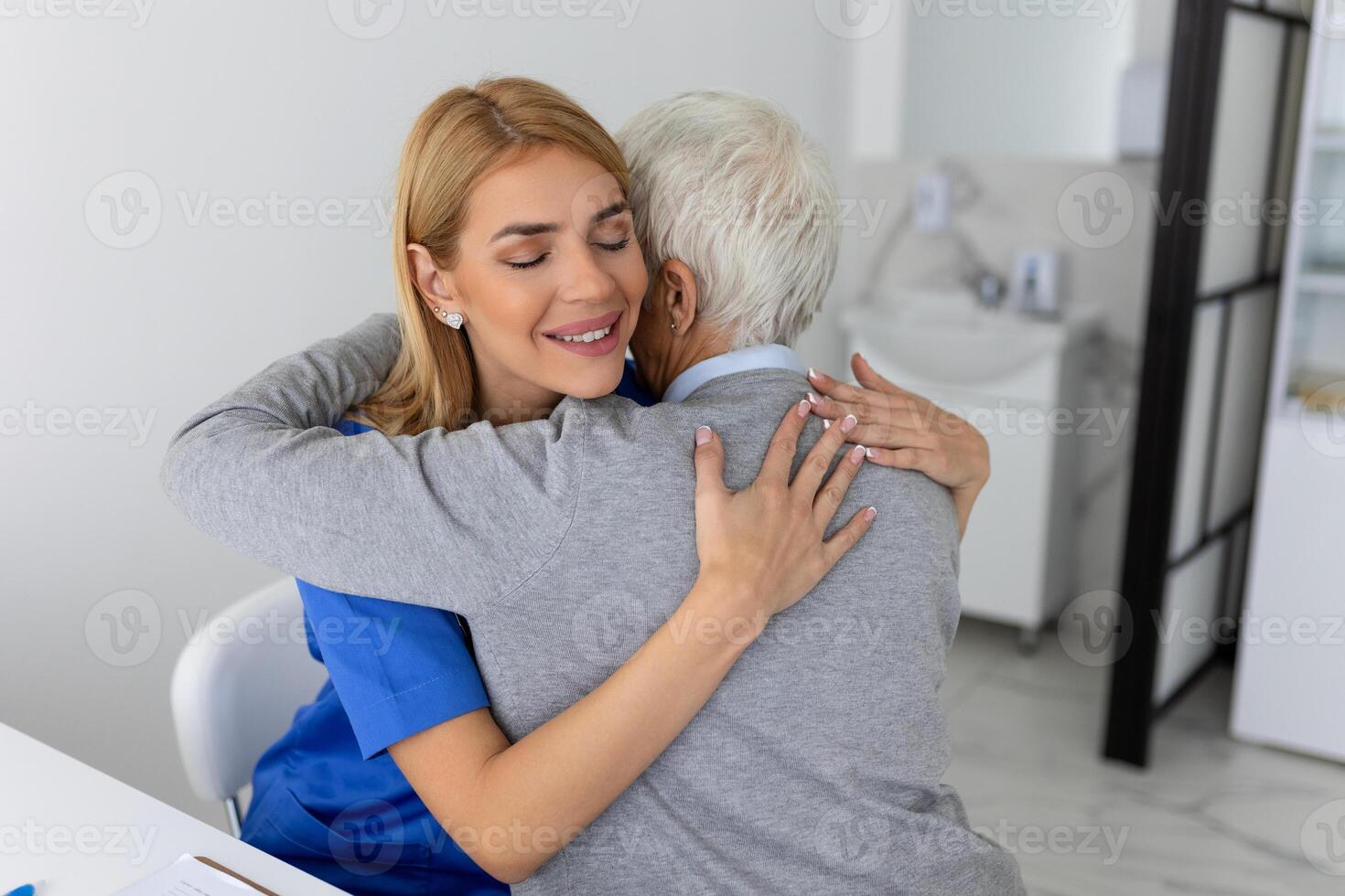 The elderly woman enjoys an embrace from her favorite healthcare doctor. Medical care, young female doctor hugging patient. Empathy concept. Elderly woman hugging caregiver photo