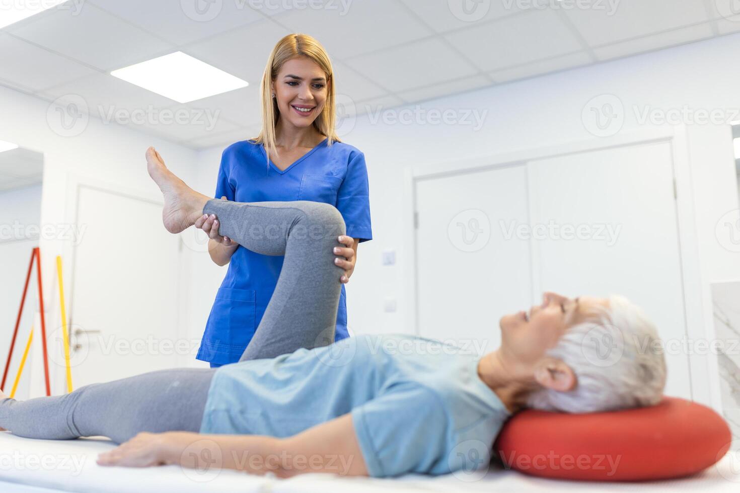 close up of female physiotherapist is helping senior elder woman stretching her hamstring and doing thigh or leg rehabilitation in exercise room - she is lying on massage bed photo