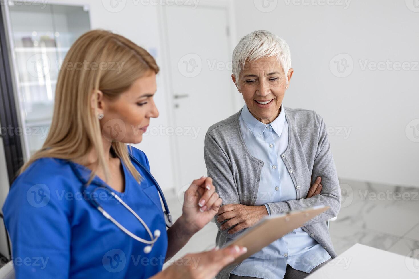 Young woman doctor or GP in white medical uniform consult senior female patient in private hospital. Female therapist speak talk with woman client on consultation in clinic. photo