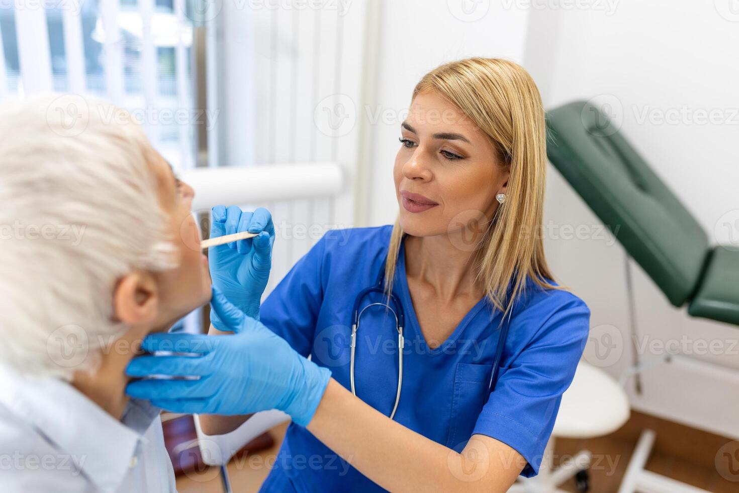 Senior patient opening her mouth for the doctor to look in her throat. Female doctor examining sore throat of patient in clinic. Otolaryngologist examines sore throat of patient. photo