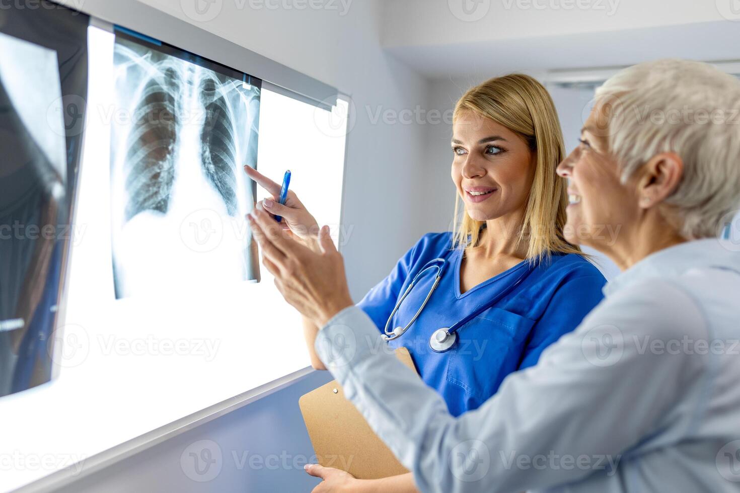Doctor woman checking x-ray film in medical laboratory at hospital, explaining the results of scan lung on screen to senior patient. photo