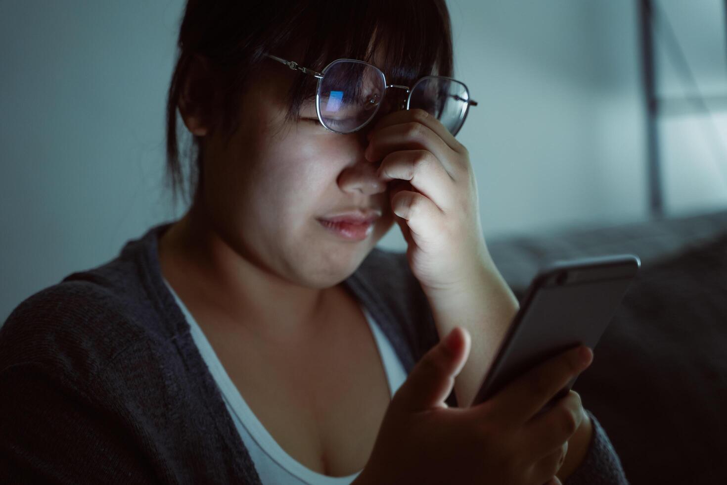 un mujer es mirando a su teléfono con su mano en su cara foto