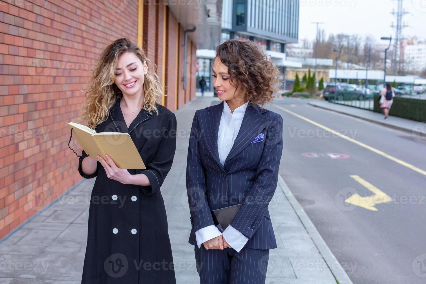 Two successful business women are talking in the city in front of a modern building. Business meeting on the street. 2 female managers with top positions. photo