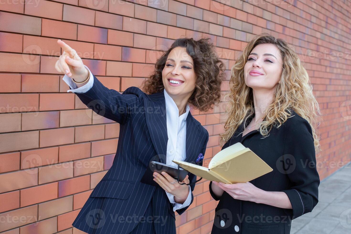 Two successful business women are talking in the city in front of a modern building. Business meeting on the street. 2 female managers with top positions. photo