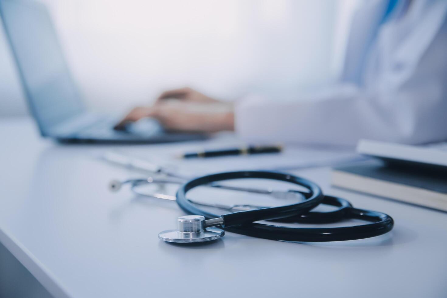 Doctor and patient sitting at the desk in clinic office. The focus is on female physician's hands filling up the medication history record form, close up. Medicine concept photo
