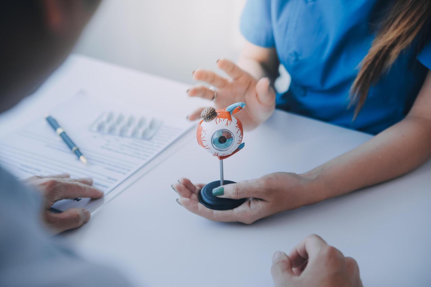 Close-up of Asian female doctor talking with elderly patient showing eyeball model and explaining eye disease in hospital photo