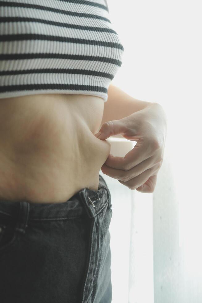 Women body fat belly. Obese woman hand holding excessive belly fat. diet lifestyle concept to reduce belly and shape up healthy stomach muscle. photo