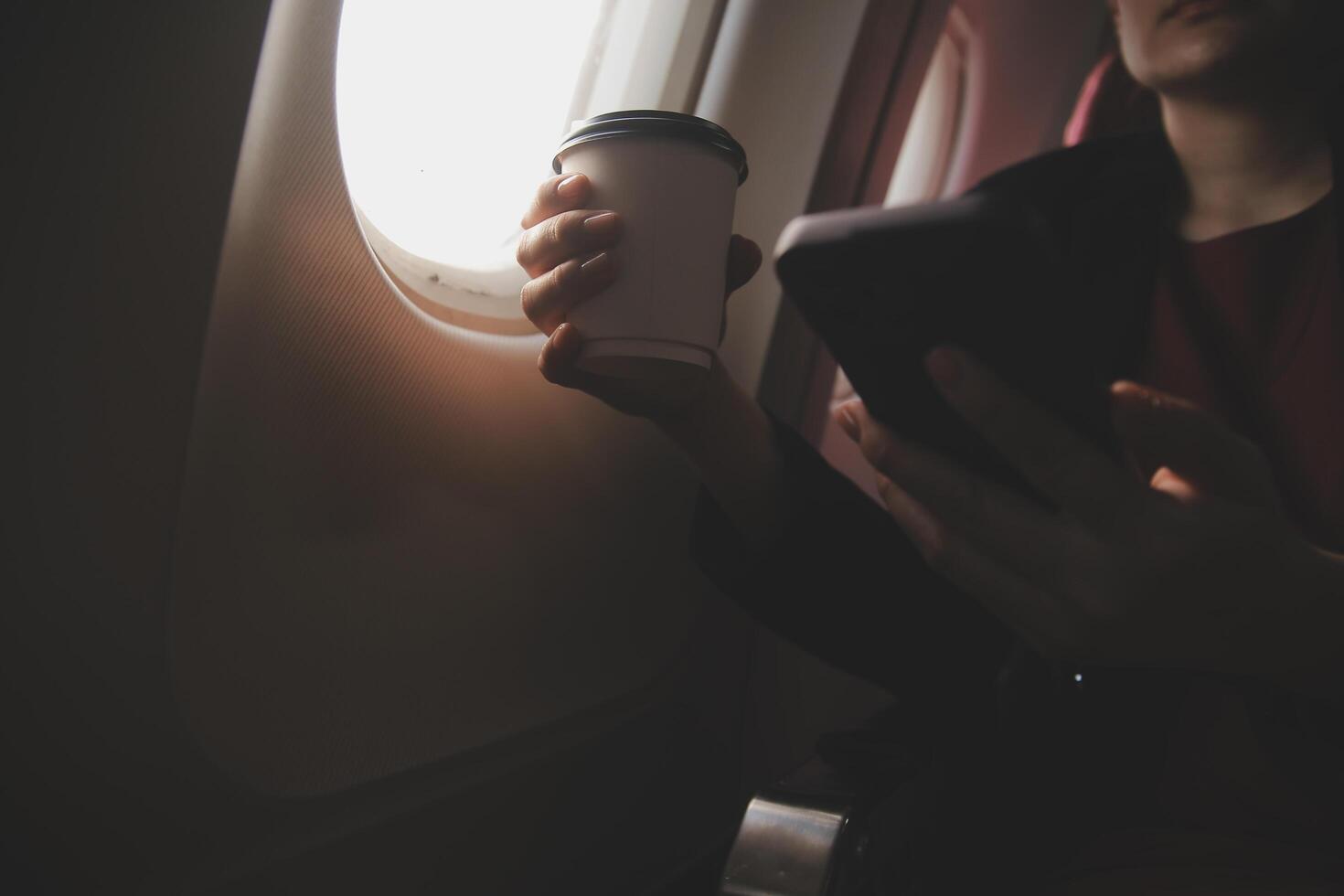Blonde female tourist checking incoming notification on smartphone sitting on seat of airplane with netbook.Young businesswoman share media from telephone on laptop computer during plane flight photo