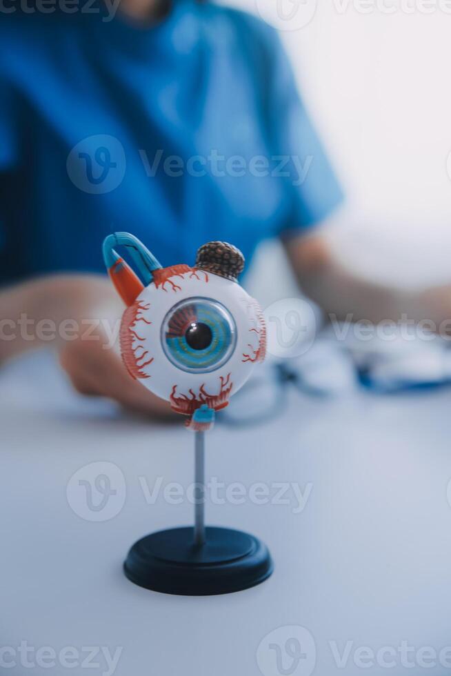 de cerca de asiático hembra médico hablando con mayor paciente demostración globo ocular modelo y explicando ojo enfermedad en hospital foto
