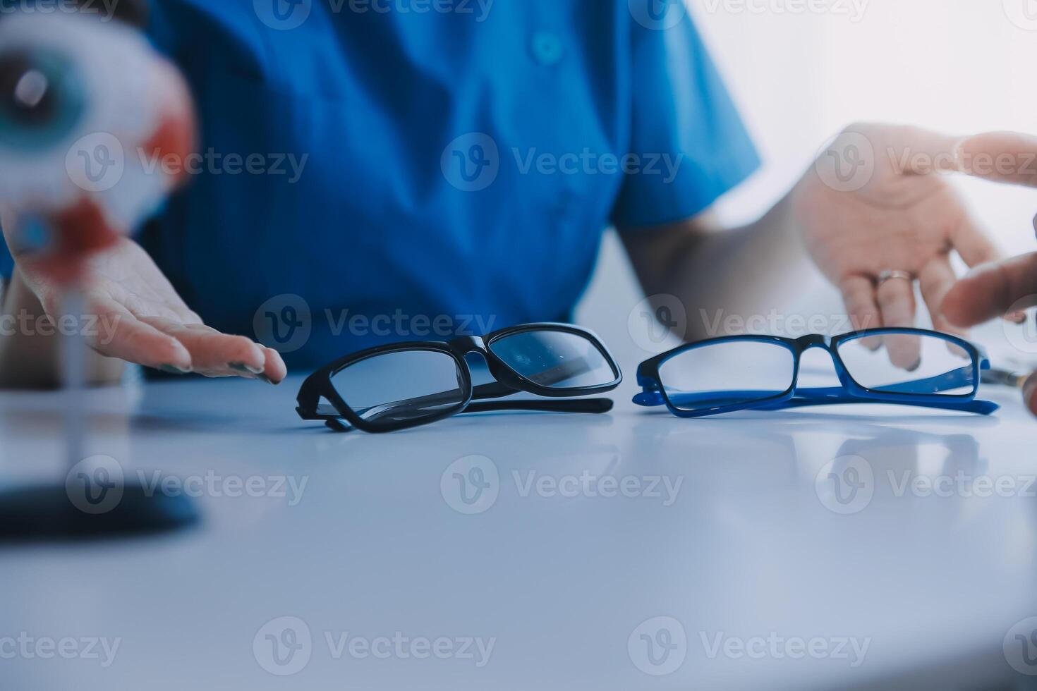 Close-up of Asian female doctor talking with elderly patient showing eyeball model and explaining eye disease in hospital photo