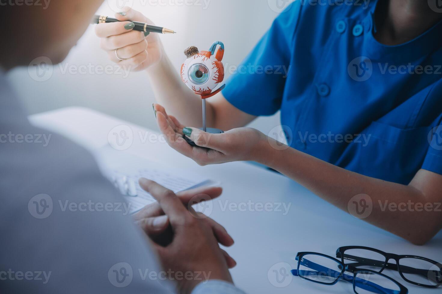 Close-up of Asian female doctor talking with elderly patient showing eyeball model and explaining eye disease in hospital photo