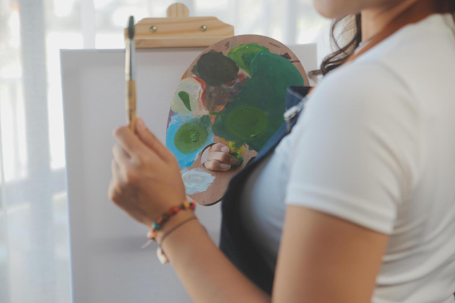 Cropped image of female artist standing in front of an easel and dipping brush into color palette photo