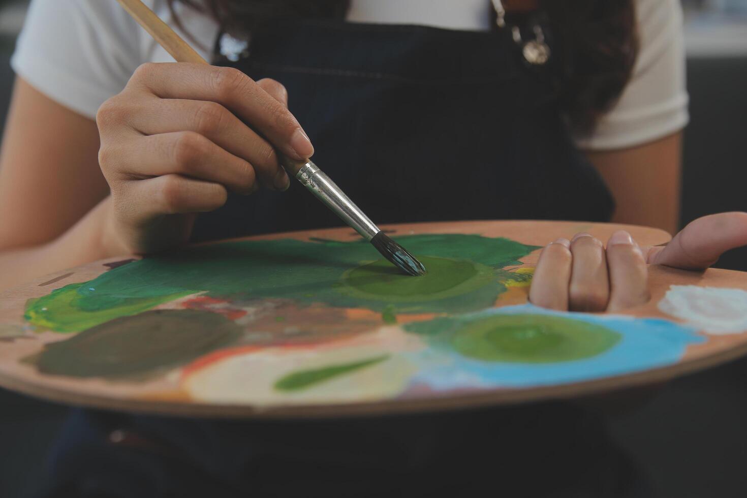 Cropped image of female artist standing in front of an easel and dipping brush into color palette photo