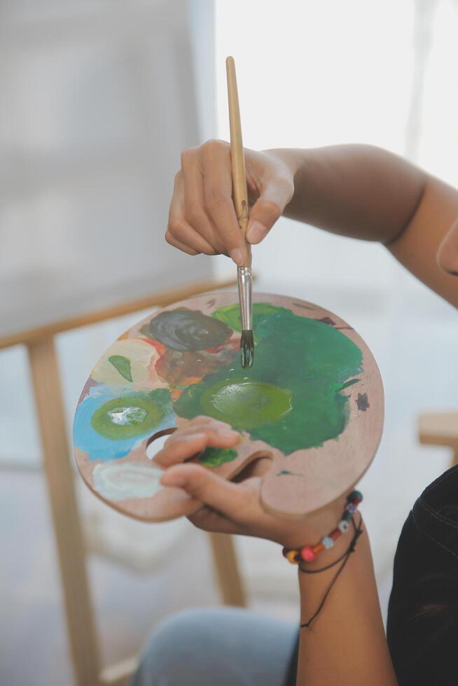 Cropped image of female artist standing in front of an easel and dipping brush into color palette photo