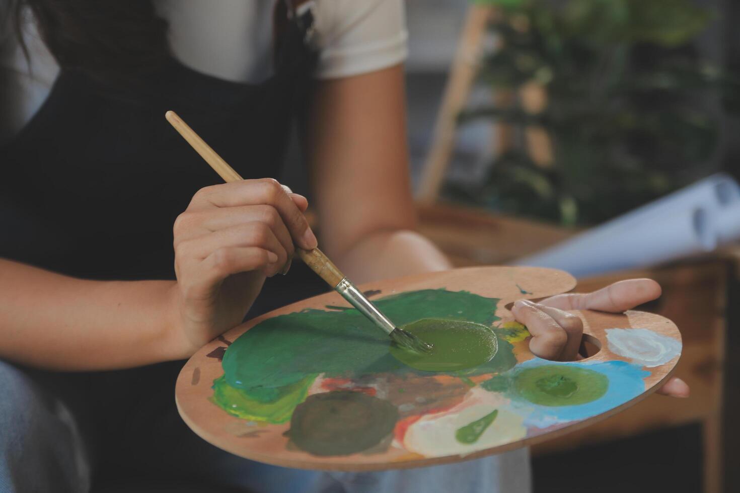 Cropped image of female artist standing in front of an easel and dipping brush into color palette photo