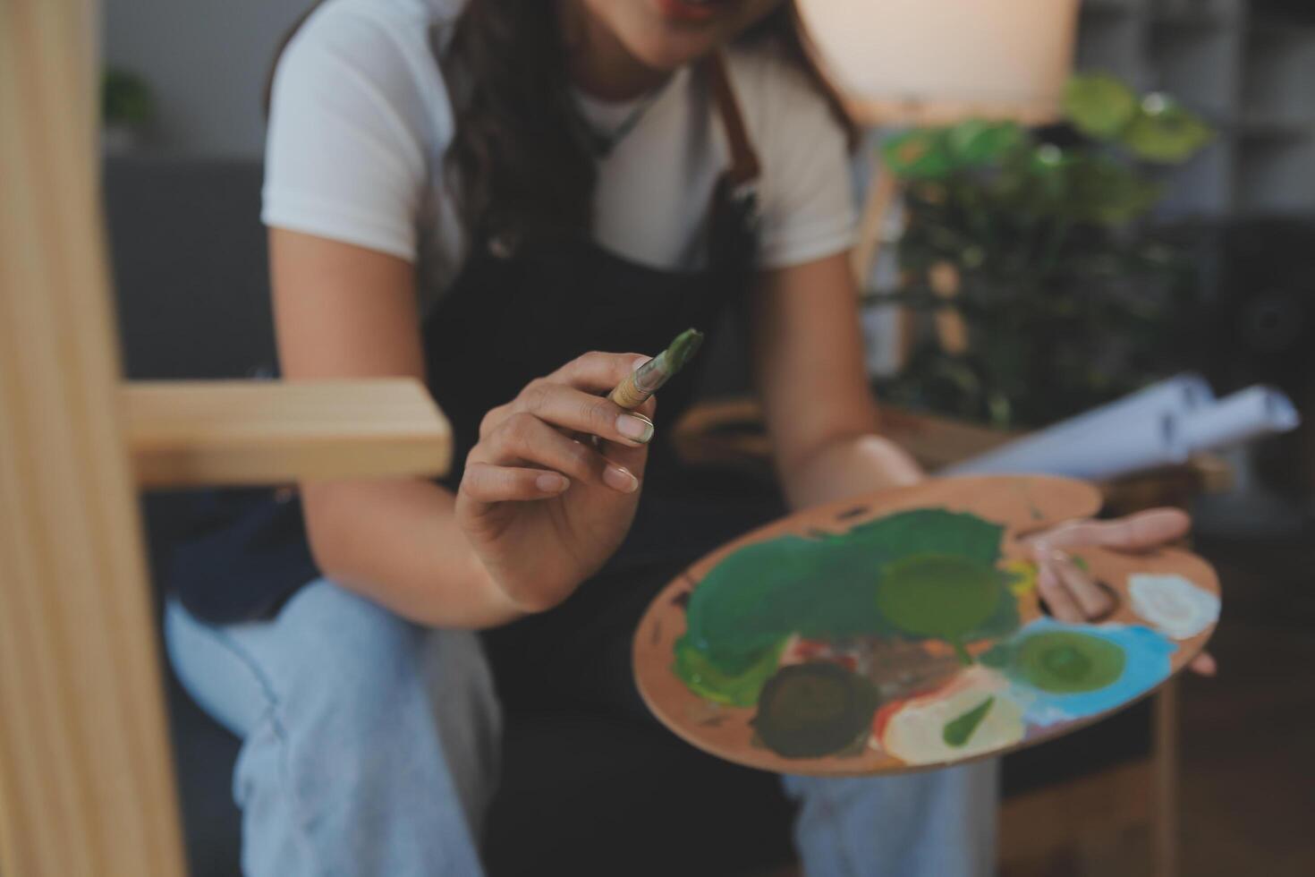 Cropped image of female artist standing in front of an easel and dipping brush into color palette photo