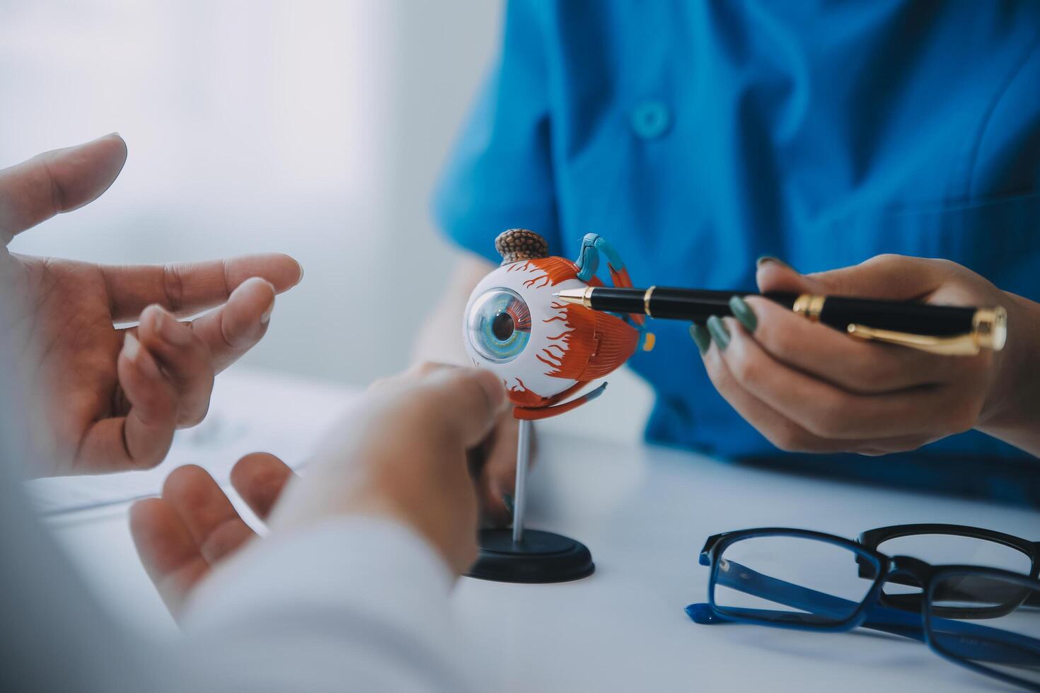 Close-up of Asian female doctor talking with elderly patient showing eyeball model and explaining eye disease in hospital photo