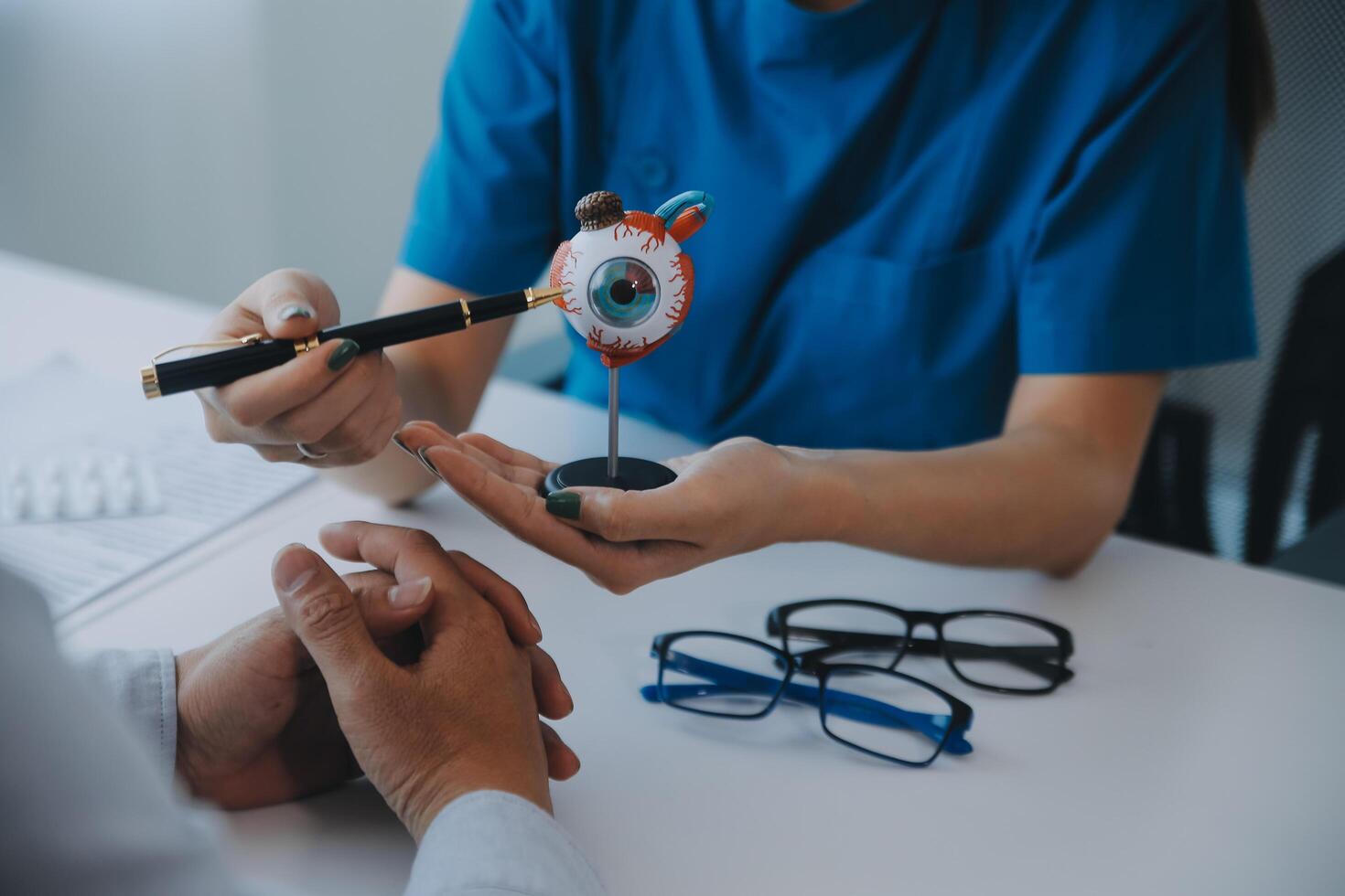 Close-up of Asian female doctor talking with elderly patient showing eyeball model and explaining eye disease in hospital photo