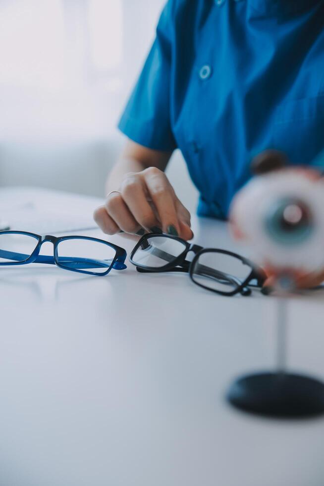 Close-up of Asian female doctor talking with elderly patient showing eyeball model and explaining eye disease in hospital photo