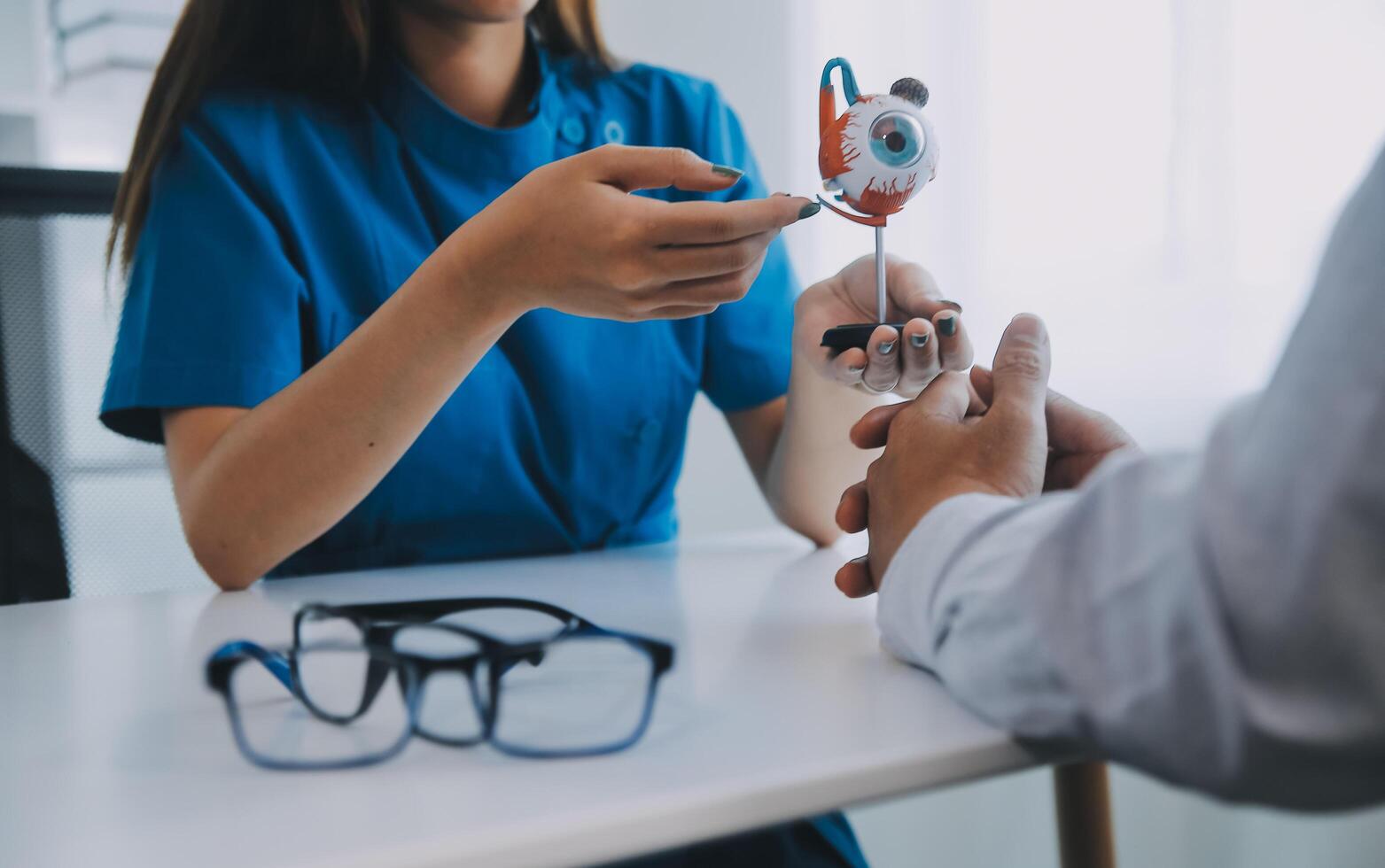 Close-up of Asian female doctor talking with elderly patient showing eyeball model and explaining eye disease in hospital photo