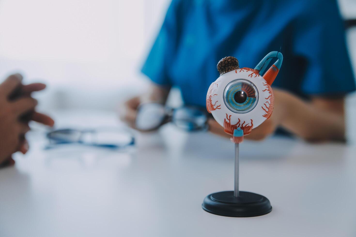Close-up of Asian female doctor talking with elderly patient showing eyeball model and explaining eye disease in hospital photo