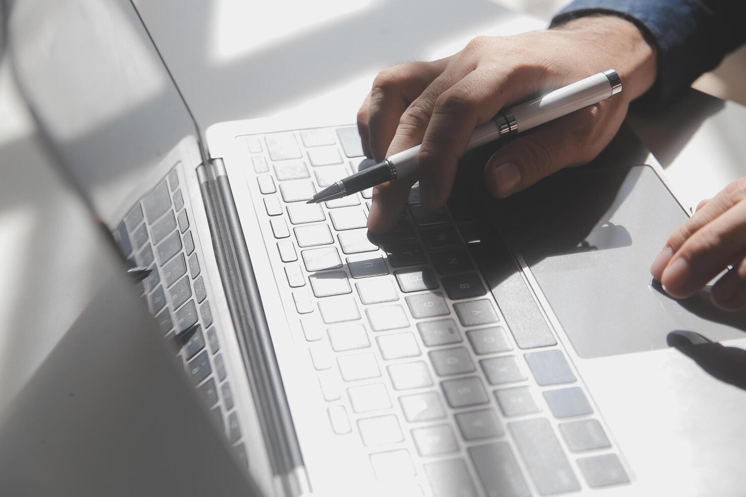 recortado imagen de un joven hombre trabajando en su ordenador portátil en un café comercio, posterior ver de negocio hombre manos ocupado utilizando ordenador portátil a oficina escritorio, joven masculino estudiante mecanografía en computadora sentado a de madera mesa foto