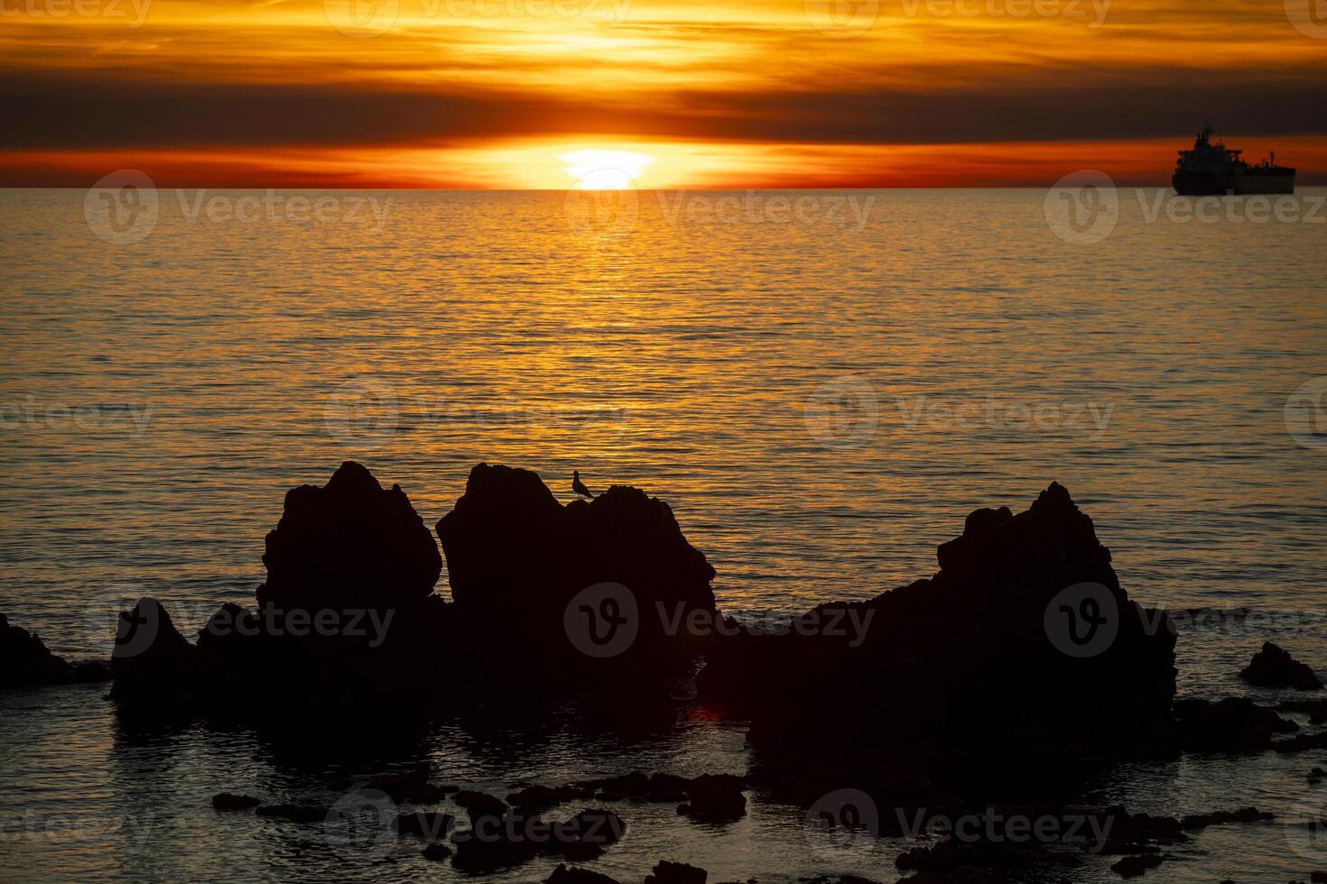Sunset over the sea with cliffs and oil tanker in the backlight photo