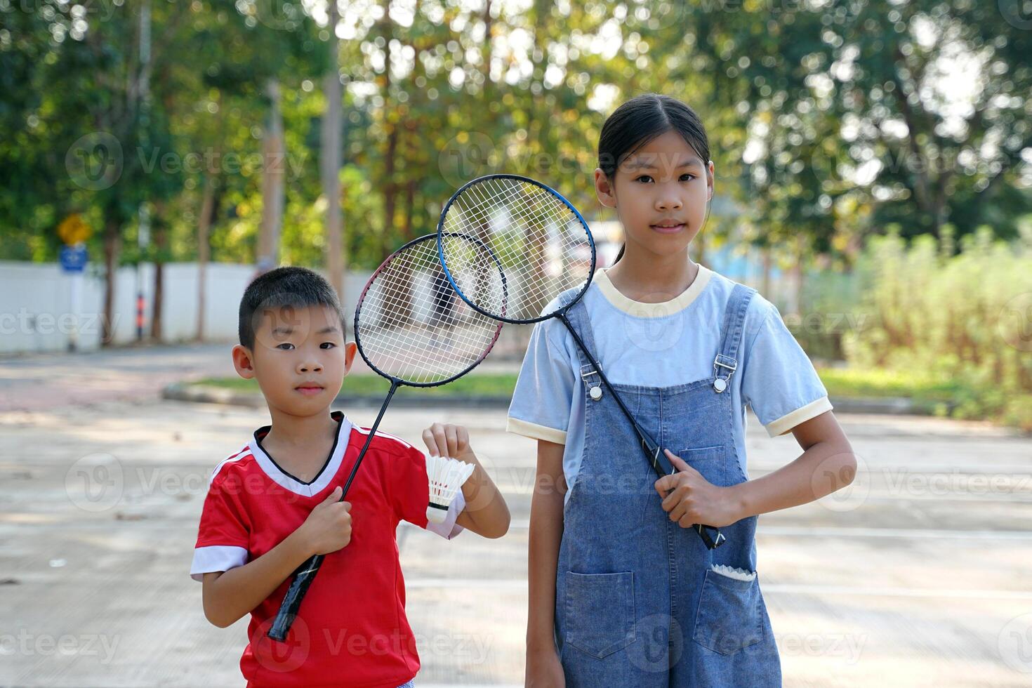 An Asian girl and boy stand together holding badminton rackets and white shuttlecocks. photo