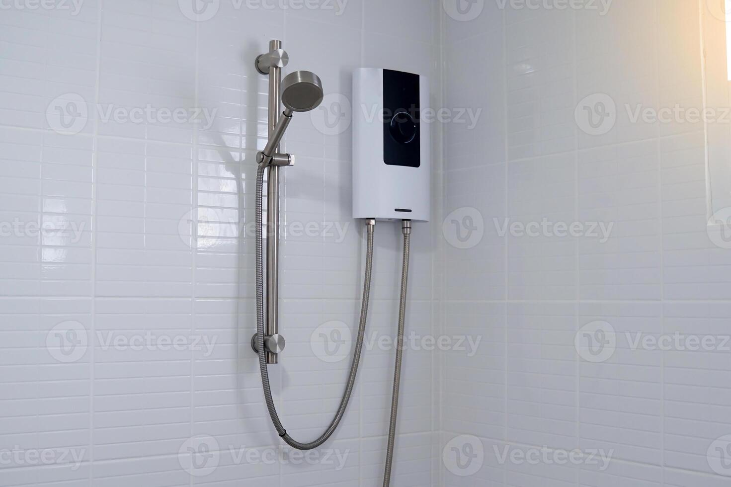 Water heater in black and white tones and a metal hand shower set mounted on a white bathroom wall. photo