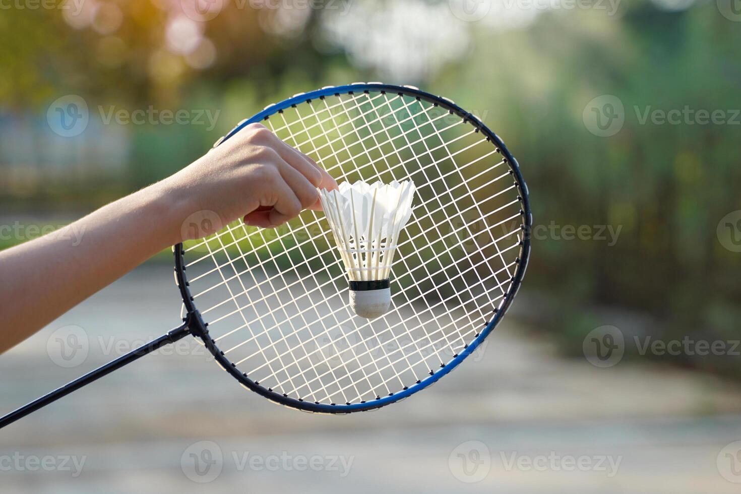 a person holding a shuttlecock in front of a badminton racket, concept for outdoor badminton playing in free times, soft and selective focus. photo